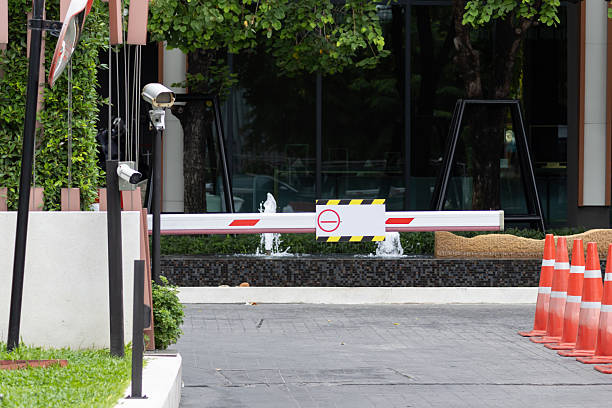 Modern security gate blocks access to private property. Barrier stands open on paved driveway. Surveillance cameras monitor entrance area. Orange traffic cones line right side