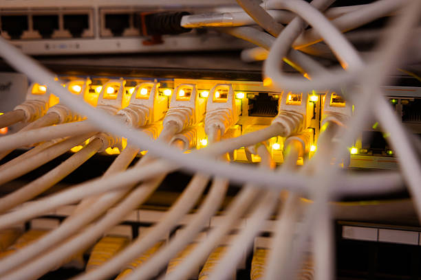 This image shows a modern network infrastructure at the heart of a data center. In the foreground is a professional network switch with numerous colored Ethernet cables neatly plugged into its ports. The cables are neatly and organized, reflecting the clean, professional appearance of a typical data center rack.