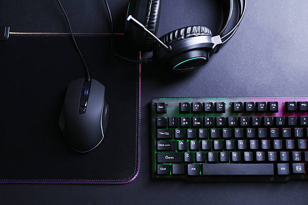Wired mouse, mousepad, computer keyboard and headset on black table, flat lay